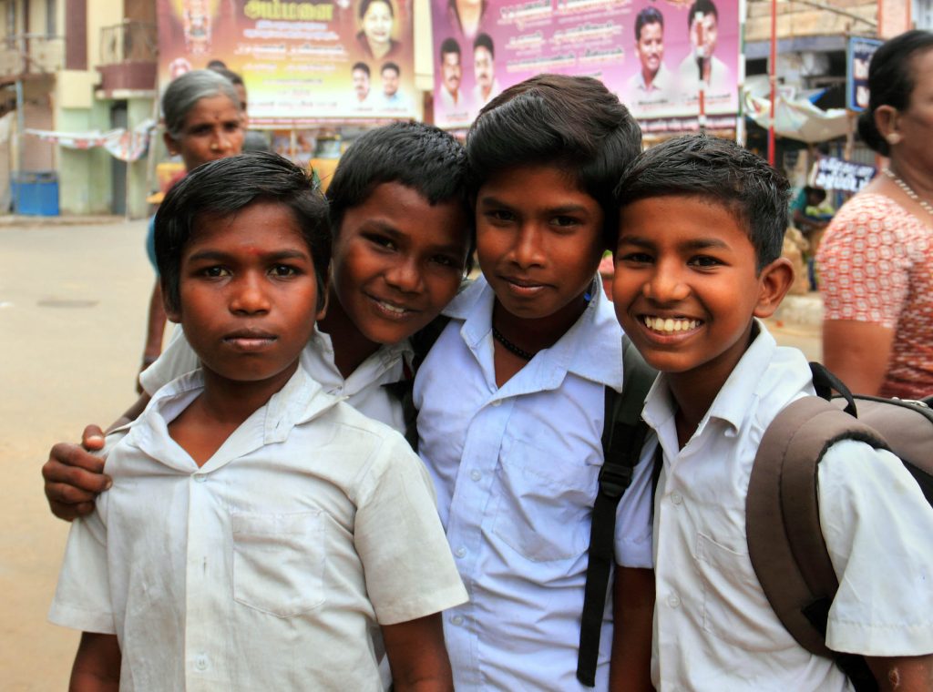 Four children stand together wearing button-up shirts, two of them are wearing rucksacks.