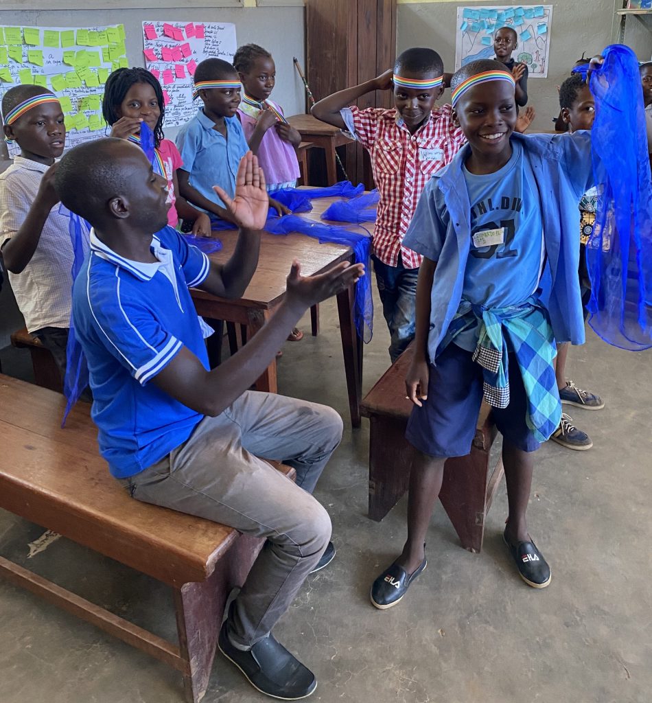 A group of children participating in health education. They have blue fabric strips and rainbow headbands.
