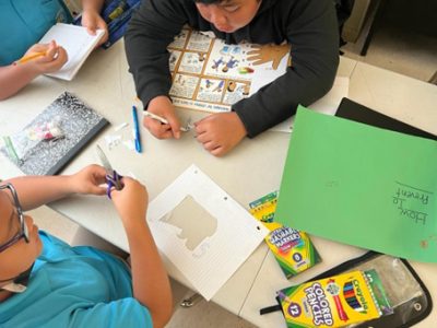 3 children are working at a table with the diabetes poster and coloured pencils, markers and paper.