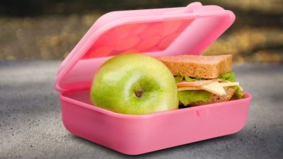 A pink lunch box with a green apple and a sandwich