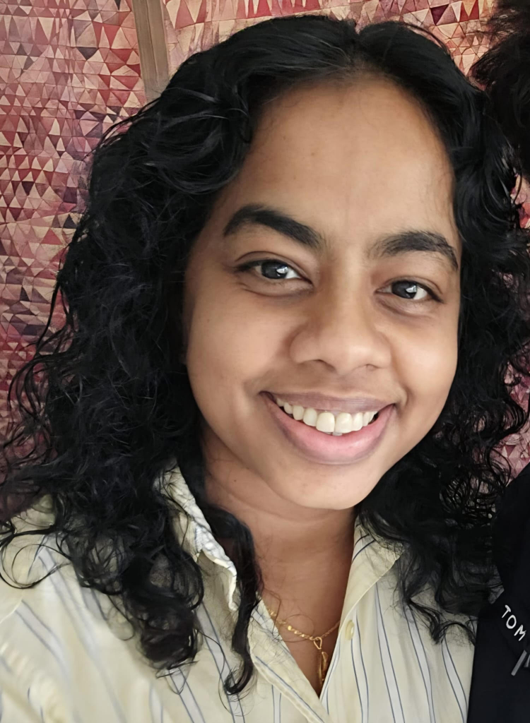 Lilanga is Children for Health's CEO. She has long, dark hair and is smiling and is wearing a gold necklace and a striped button down shirt.